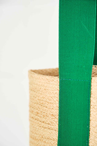 This long and tapered tote is stitched from a 5/16” raffia tape sewn edge to edge for flexibility. A small inside pocket will hold a phone and credit cards. The 1 5/8” emerald green elastic handle straps stops halfway down the bag, and a natural leather handle narrows the strap for a better hold. This bag can be carried over the shoulder, and when loaded, the elastic straps make it bounce along.