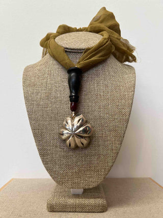 A unique necklace made from an accessory found by the designer herself at an antique market: a silver-plated flower-shaped sprayer. The khaki-coloured chiffon necklace bears a pendant formed from a piece of turned black wood (an element of a pipe), an oval red amber bead and the silver-plated flower-shaped sprayer. 